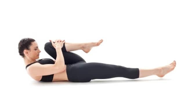 Young slender female is lying at wind relieving pose. Athletic brunette  woman in black uniform is practicing yoga, meditating in pavanamuktasana  posture at fitness studio. Healthy lifestyle concept. Stock Photo | Adobe